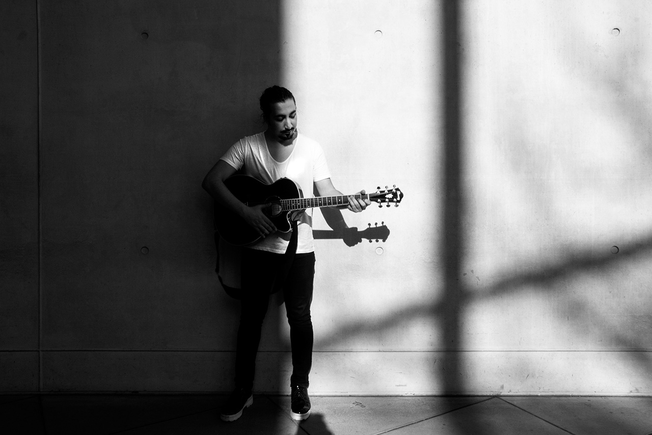 Mann vor Hauswand mit Gitarre in der Hand